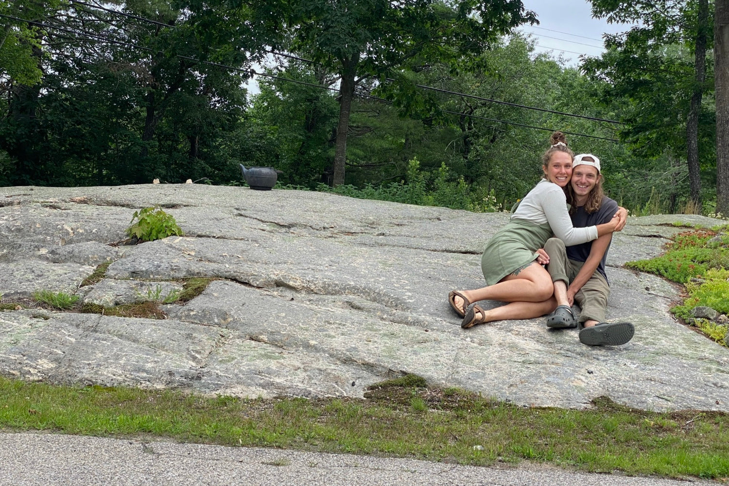 Joe and Jillian Hedglin, a young white couple, excitedly sit on a shallow rock ledge that lines the driveway to the workshop for Little Ledge Woodworks.
